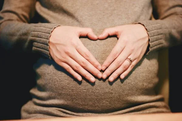 Close-up of a pregnant woman cradling her belly with hands forming a heart shape.