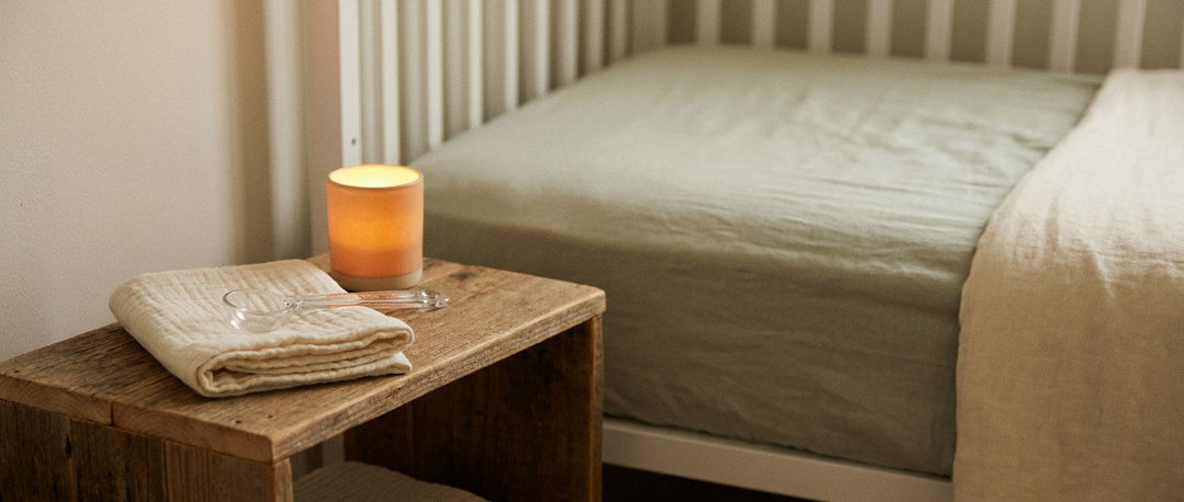 Quiet nursery at night with a muslin cloth, a clear measuring spoon and a glowing night light beside a crib